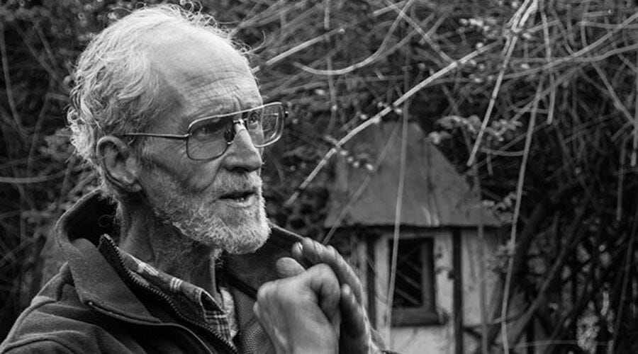 B&W photo of Ted Trainor standing in a forest.  